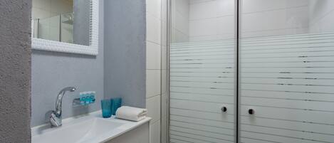 Une salle de bain avec un lavabo blanc, un miroir et une cabine de douche en verre.