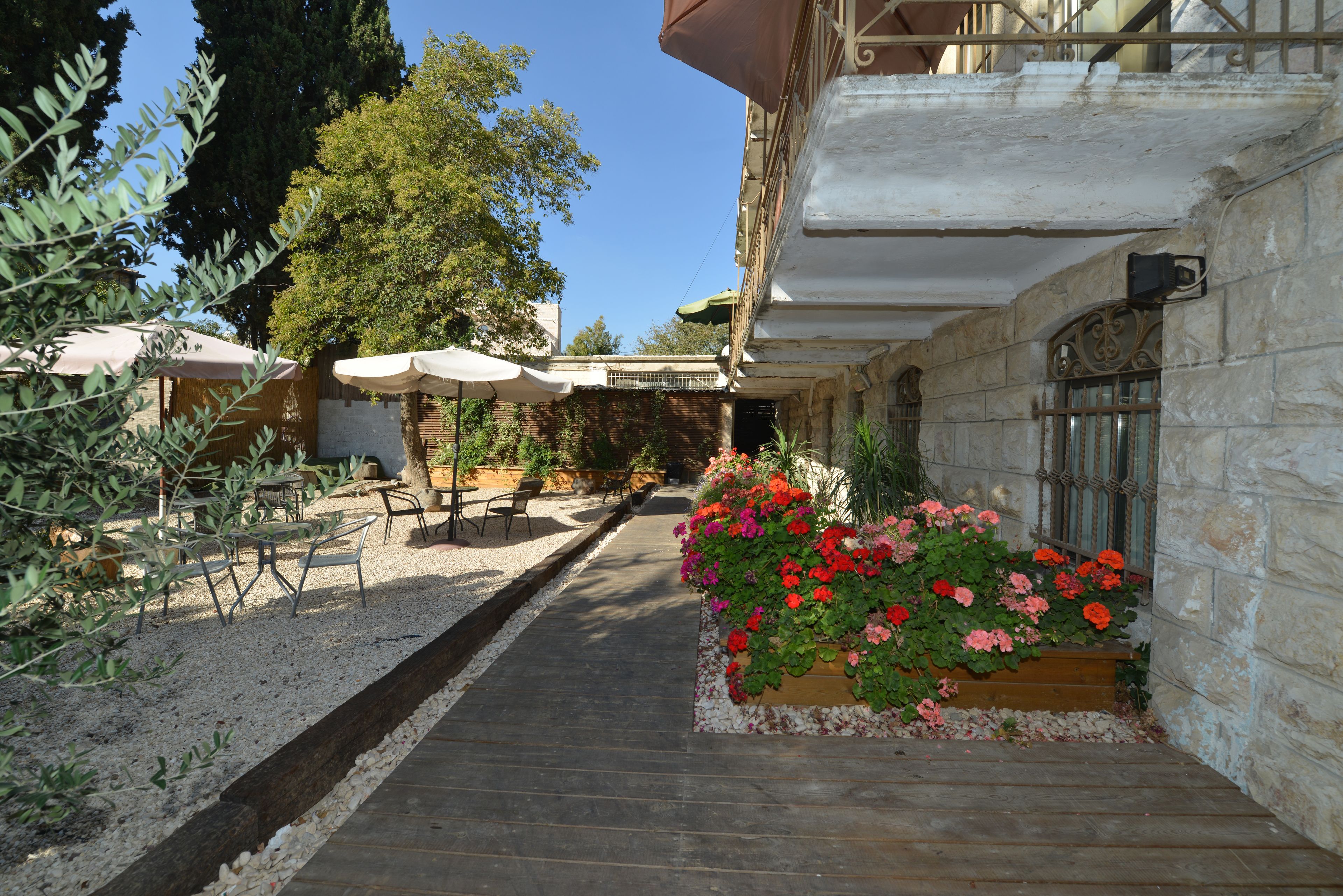Un patio con mobiliario exterior, un parterre de flores y un edificio con muros de piedra.