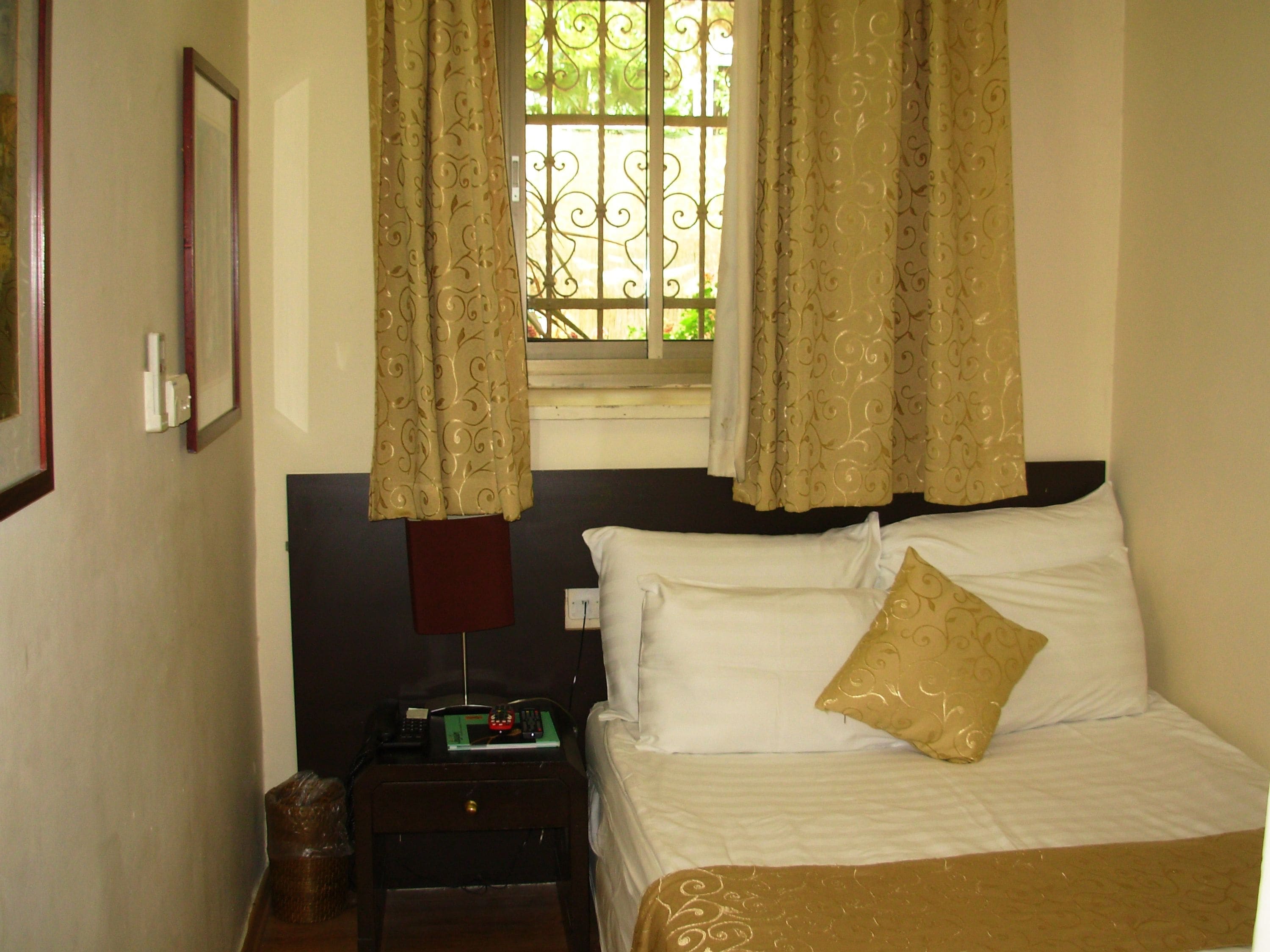 Una habitación de hotel con una cama, una mesita de noche, una lámpara y una ventana con cortinas.