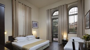 Una habitació d'hotel amb un llit gran, una taula de nit, una cadira, una finestra amb cortines i vista a l'exterior.