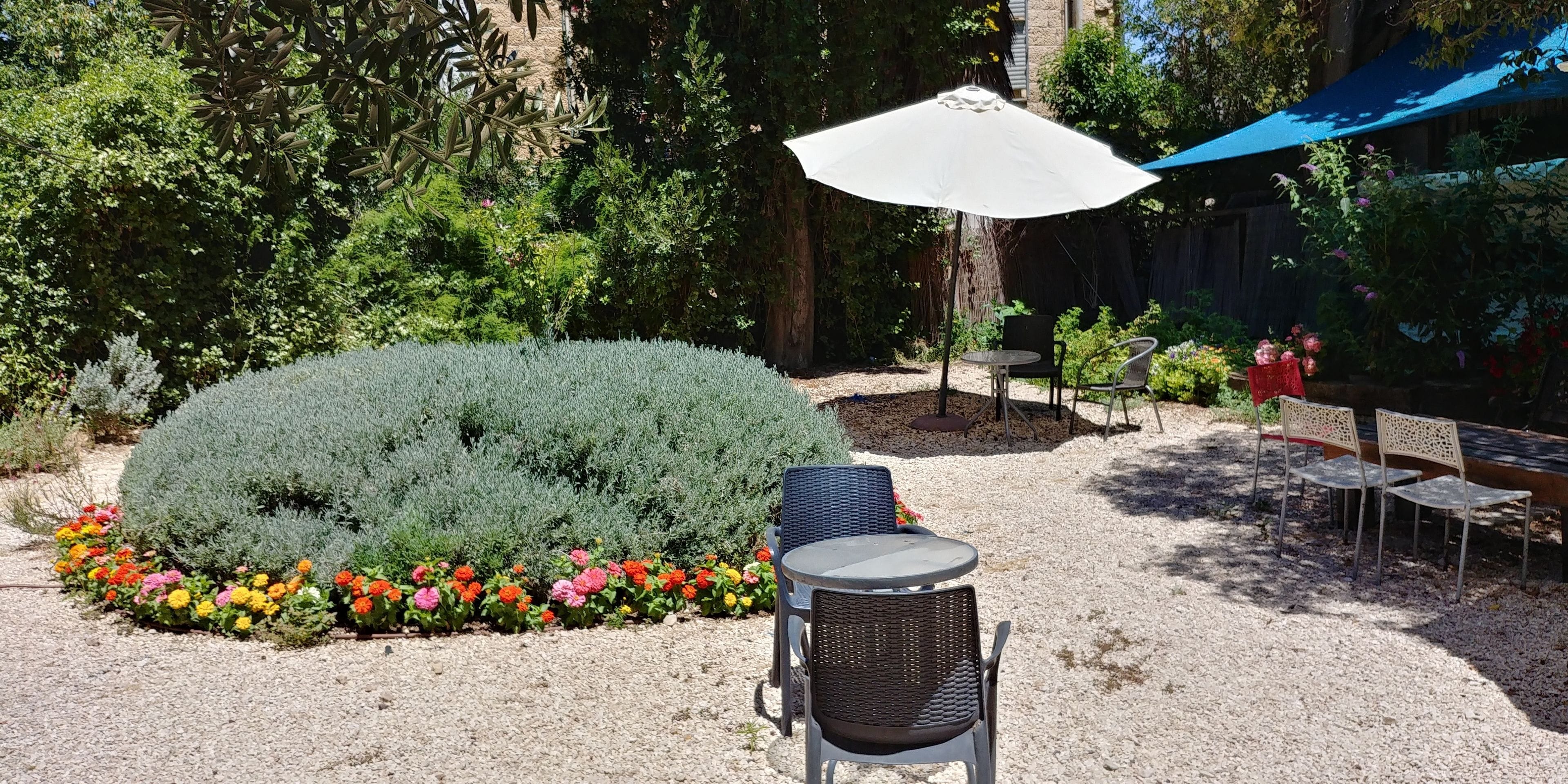 An outdoor patio area with a round table and two chairs, surrounded by a gravel path and colorful flower beds.