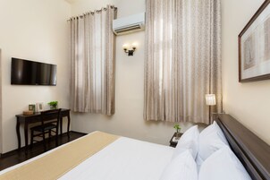 Habitación de hotel con cama, escritorio con silla, televisor montado en la pared, aire acondicionado y cortinas.