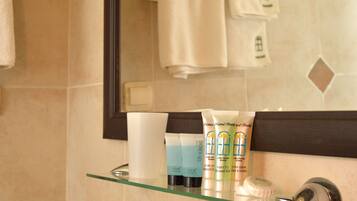 A bathroom with a glass shelf holding toiletries, a mirror, and a towel rack.