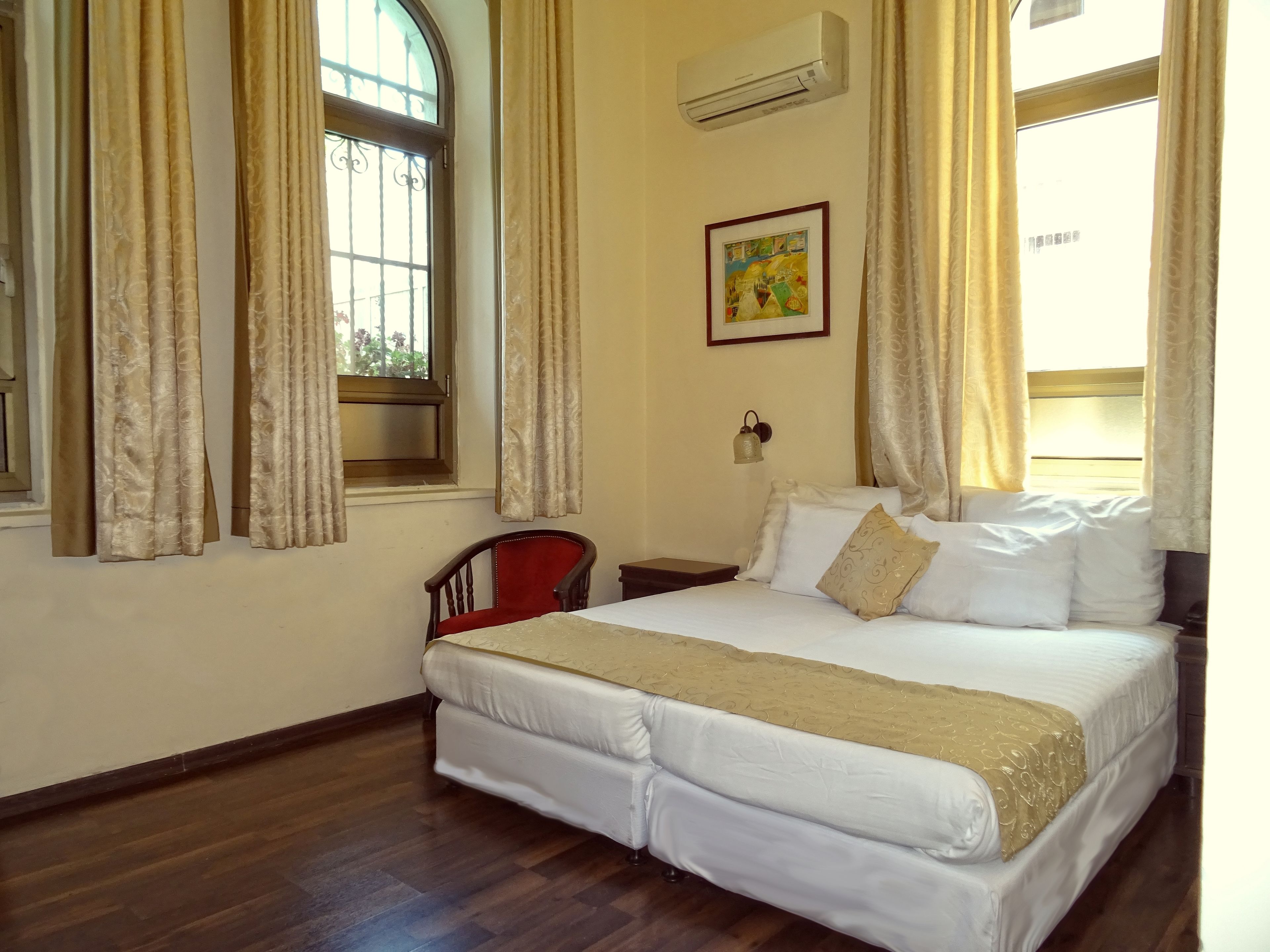 Una habitación de hotel con una cama grande, una silla, una mesita de noche y una lámpara fijada a la pared.