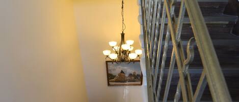 A staircase with a metal railing, a chandelier, and a framed picture on the wall.
