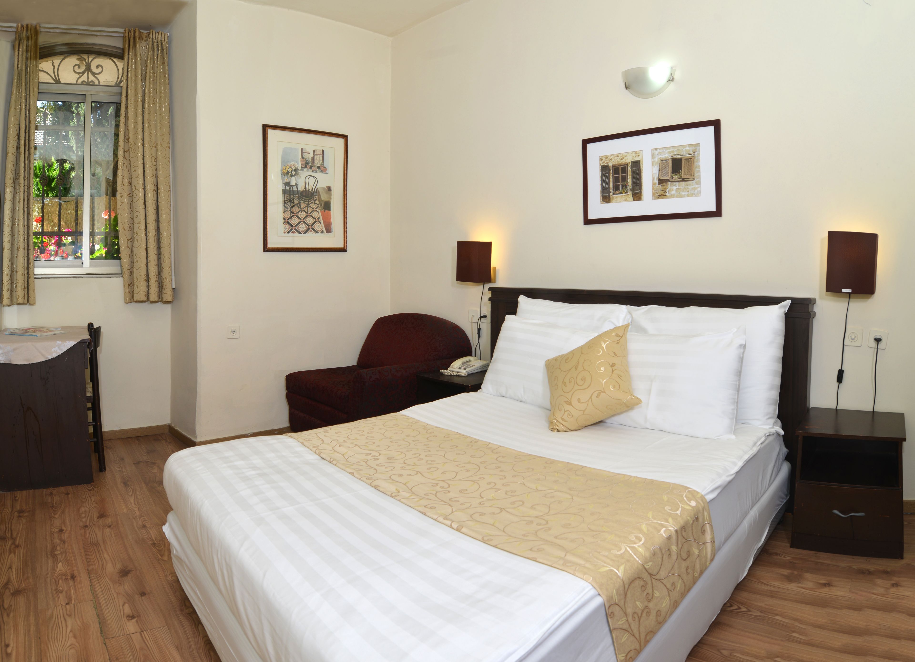 Quarto de hotel com uma cama grande, uma escrivaninha, uma cadeira e duas fotos emolduradas na parede.