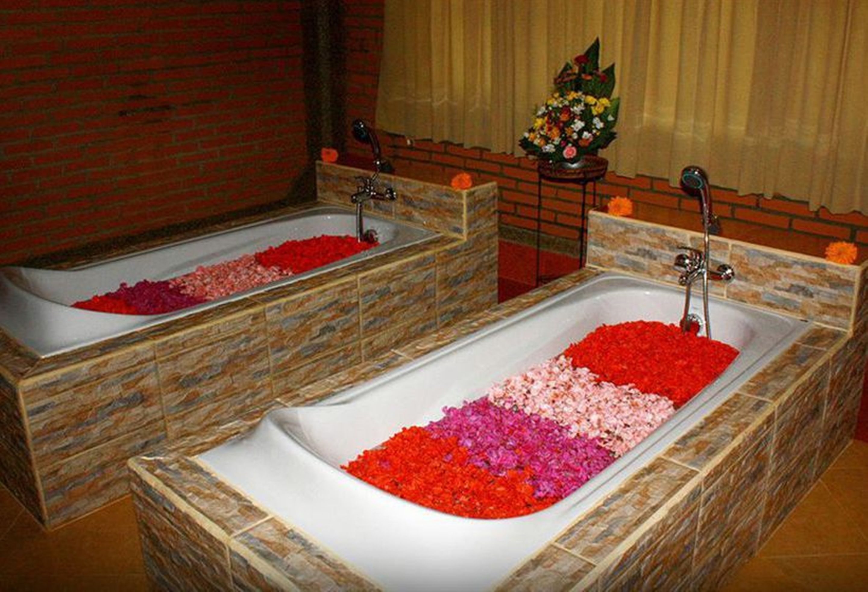 Two spa tubs filled with rose petals, set against a brick wall with a floral arrangement on a side table.