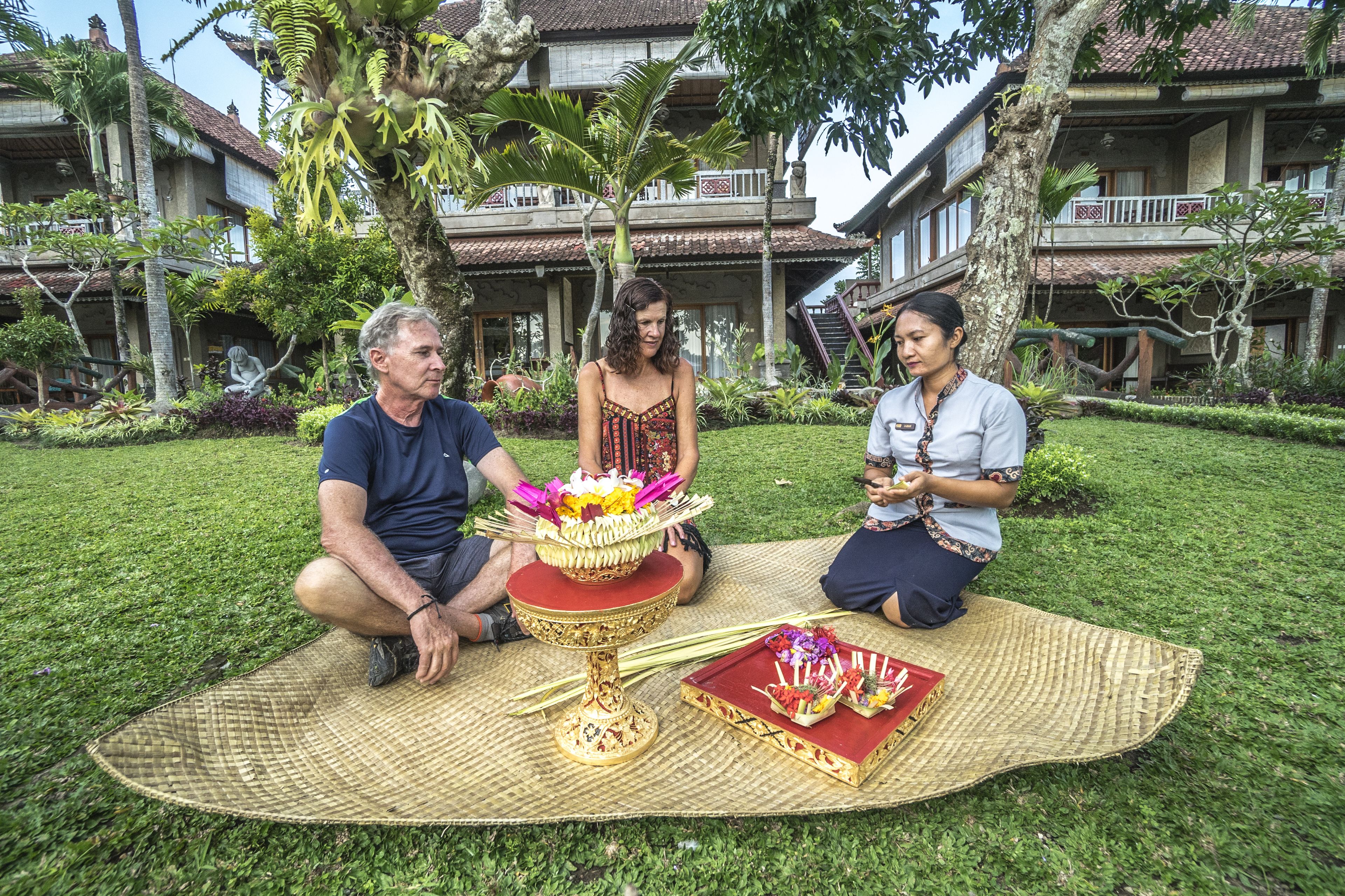 A traditional ceremony with a woven mat, a golden tray with flowers, and a statue in a lush garden setting.