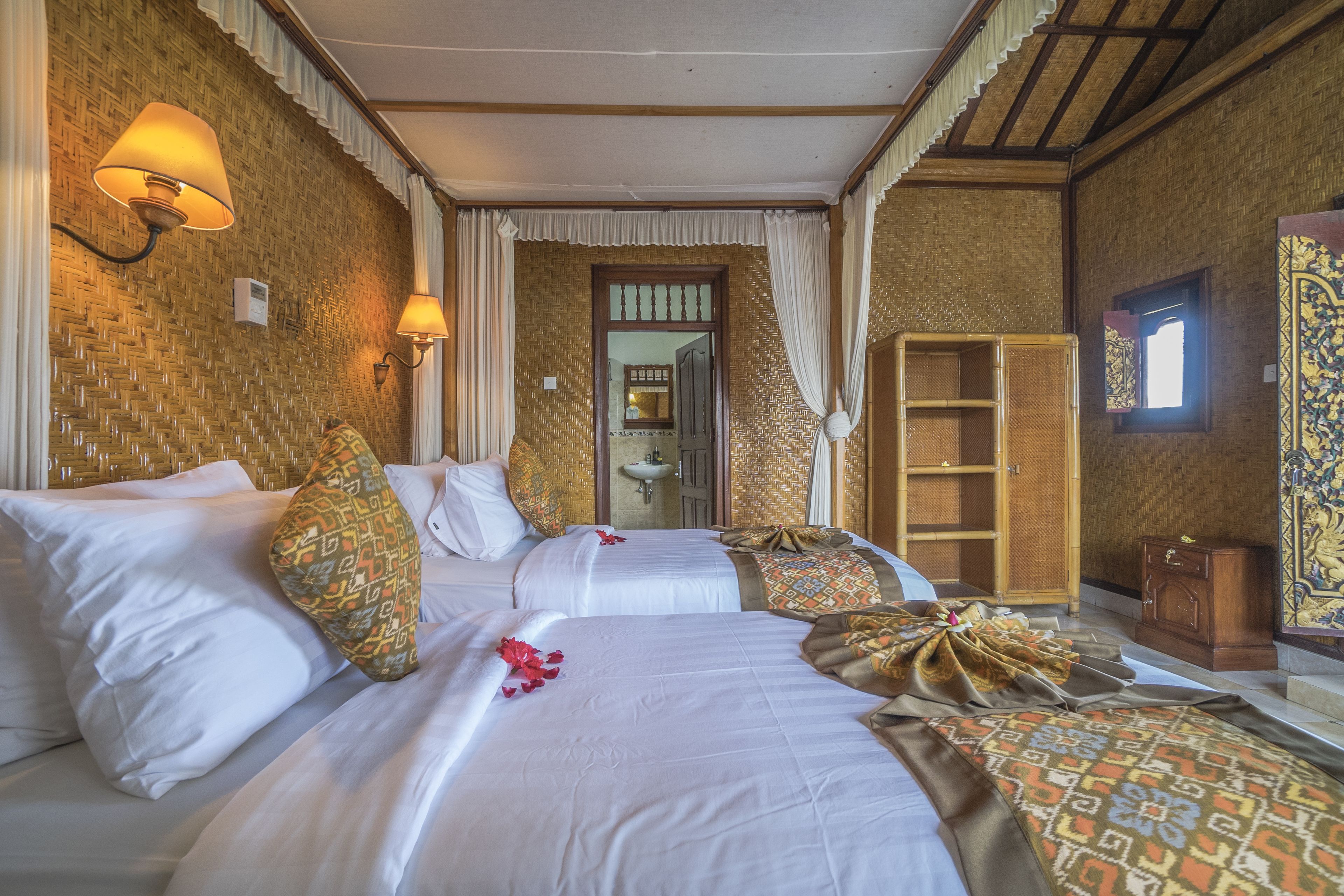 A hotel room with two beds, a mirror, a wardrobe, and a bathroom visible through an open door.