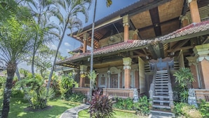 A traditional building with a staircase leading to a covered upper level, surrounded by lush greenery and palm trees. - Cendana Resort & Spa (Ubud)