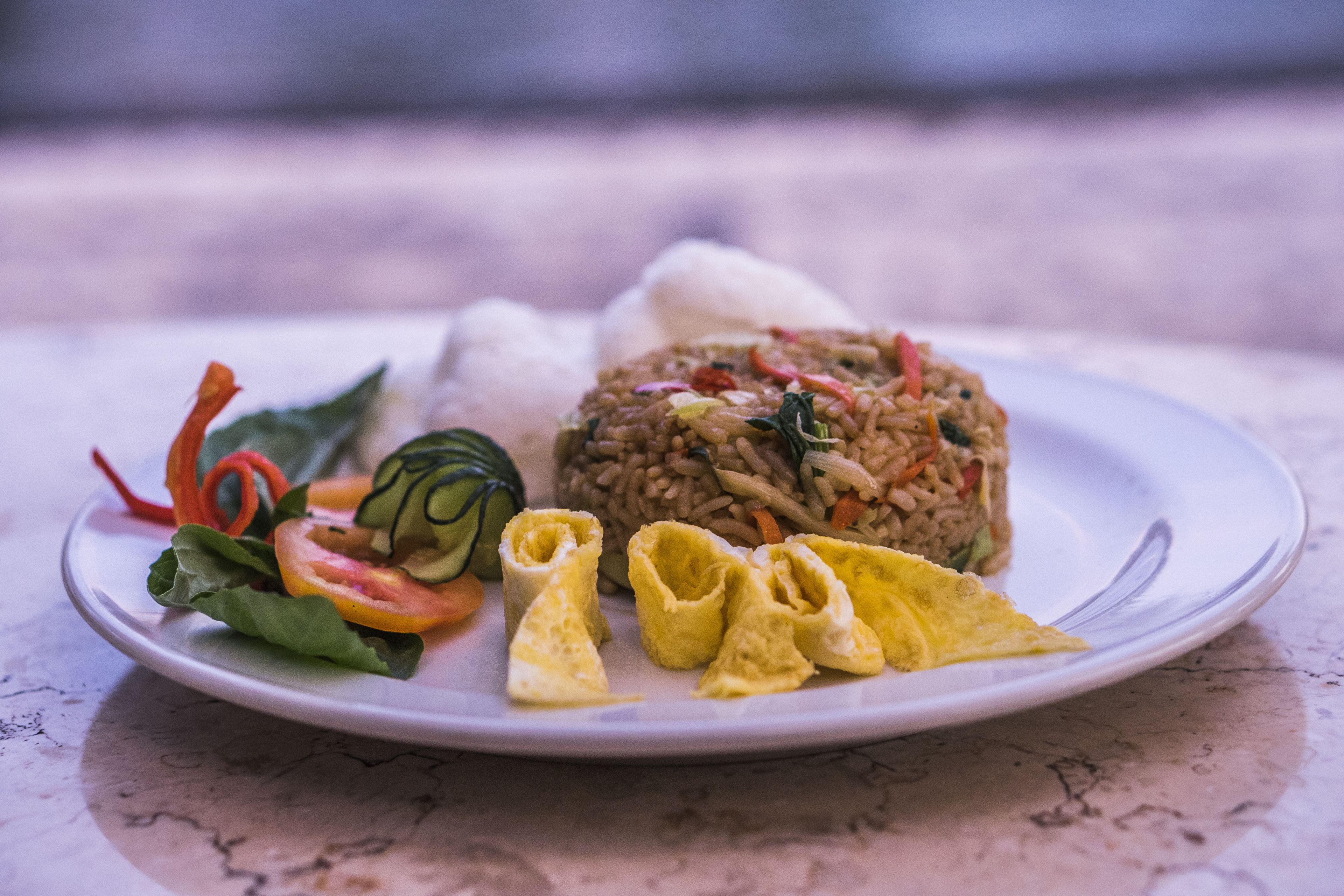 A plate of food with rice, vegetables, and a rolled omelette.