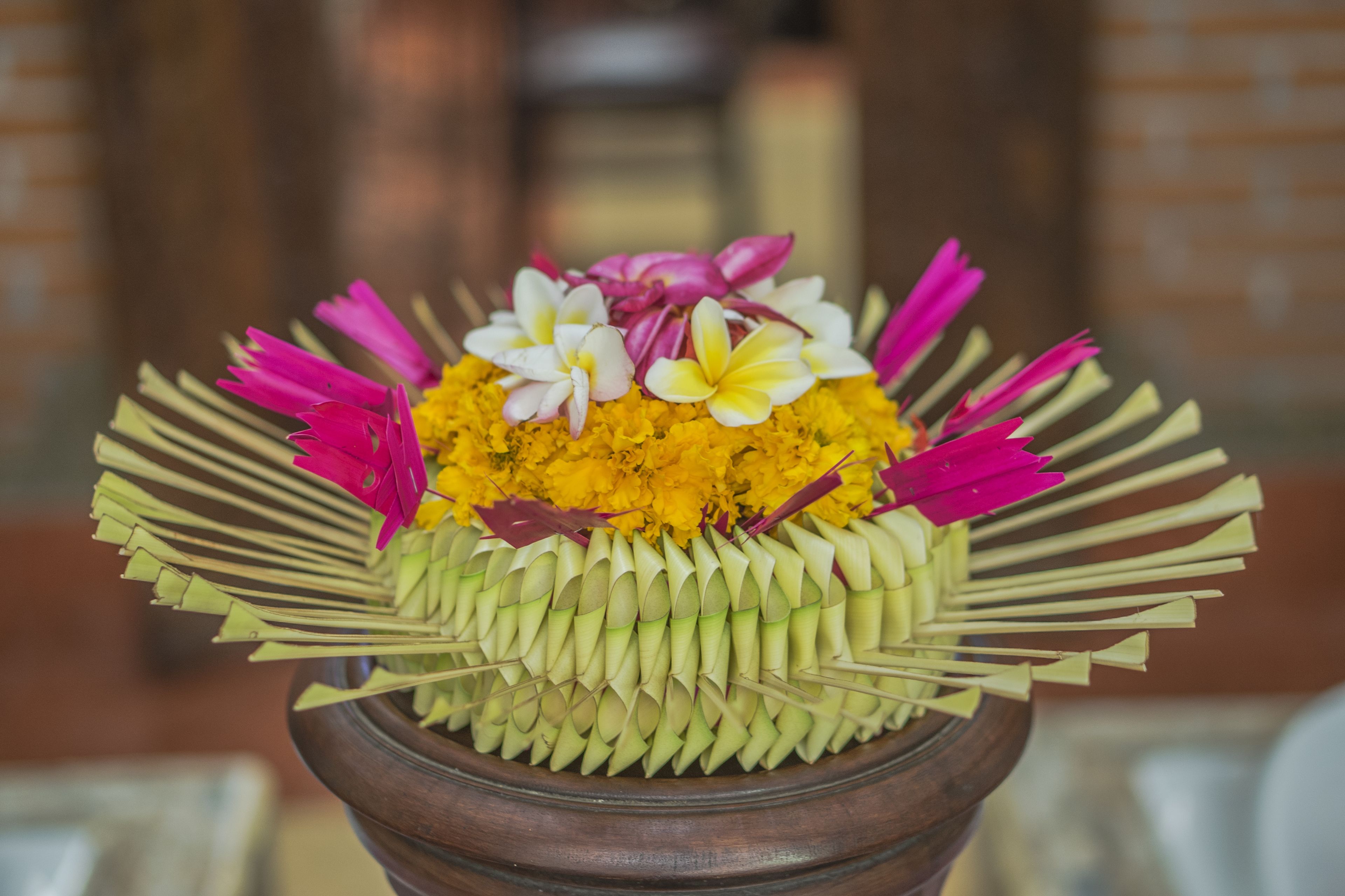 Un vase en bois orné d’un arrangement floral composé de fleurs jaunes et roses, peut-être des œillets d’Inde et des frangipaniers.