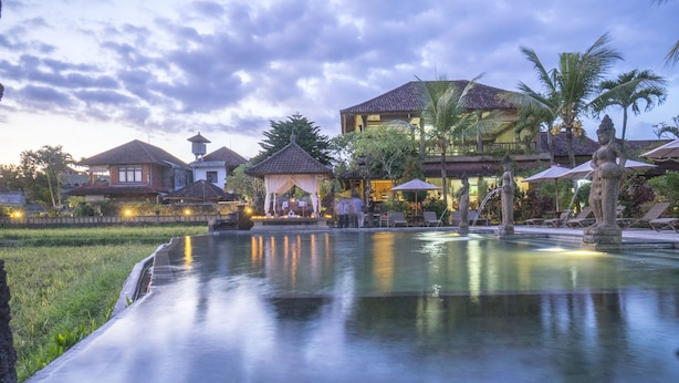 A serene pool area with a gazebo, palm trees, and a building with a tiled roof. - Cendana Resort & Spa (Ubud)
