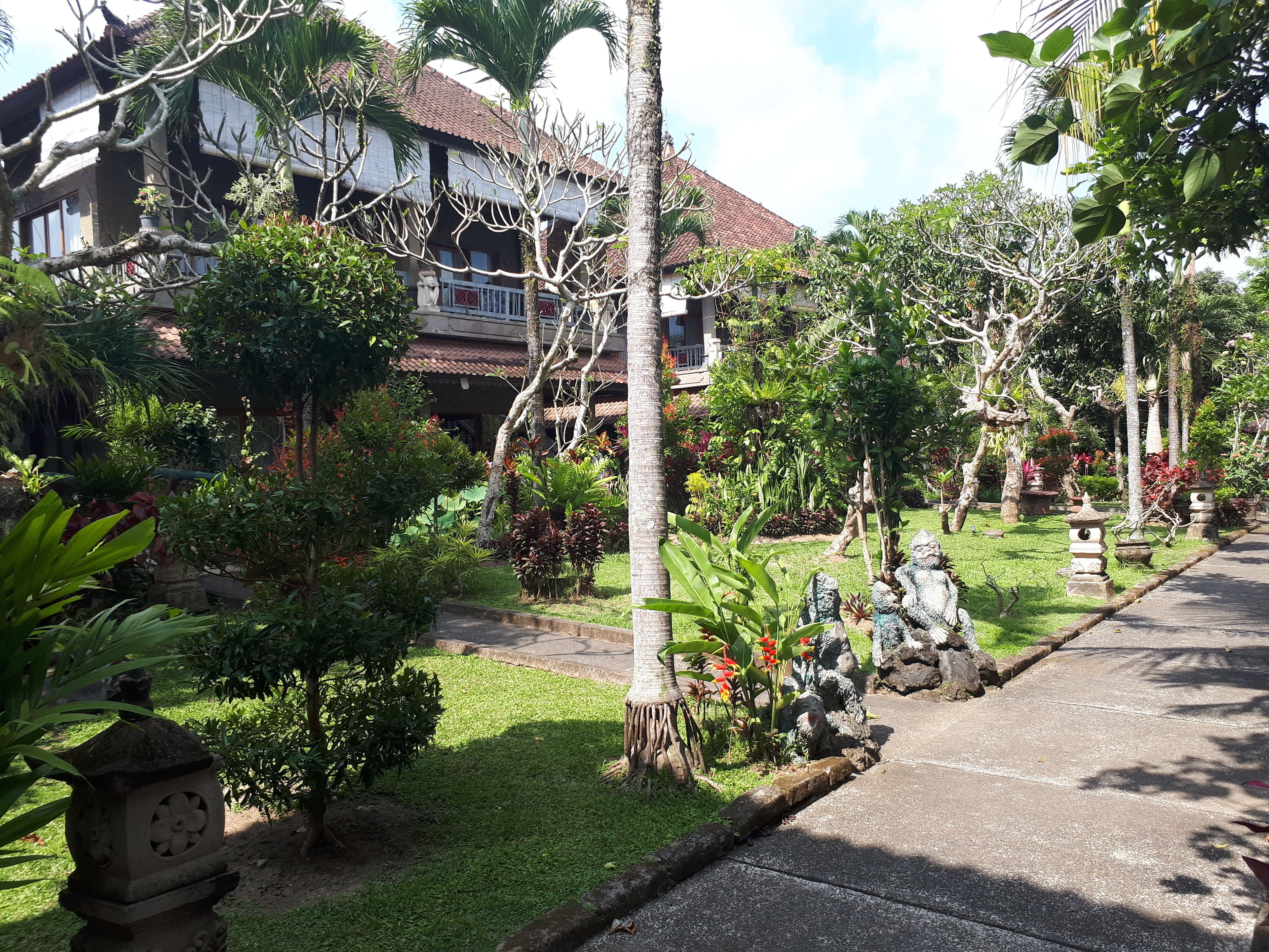 A garden with a pathway, stone lanterns, and a building with a tiled roof.