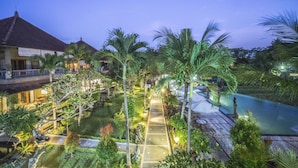A resort with a swimming pool, palm trees, and a well-lit pathway leading to the pool area. - Cendana Resort & Spa (Ubud)