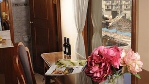 A hotel room with a dining table, a vase of flowers, and a view of a historic building. - Del Prado Inn (Cusco)