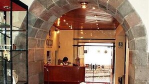 An interior corridor with a stone archway, a reception desk, and a red carpet leading to a door. - Del Prado Inn (Cusco)