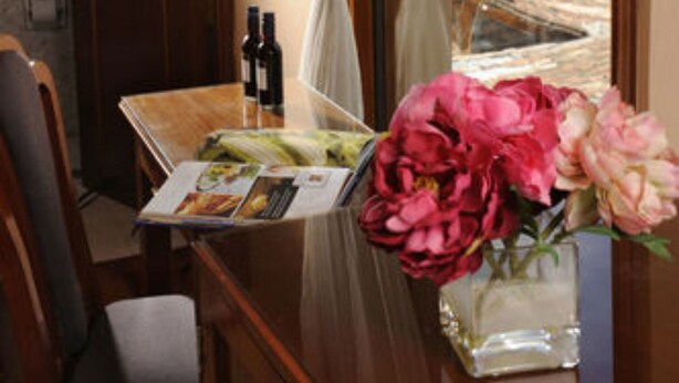 A room with a wooden table, a chair, a vase with flowers, and a window with a view of a building. - Del Prado Inn (Cusco)