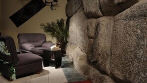 A living room with a large rock wall, a sofa, a coffee table, and a potted plant. - Del Prado Inn (Cusco)