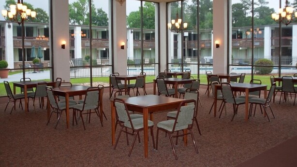 A spacious indoor dining area with multiple tables and chairs, large windows offering views of a building and greenery outside. - The Landmark Inn (Hartsville)
