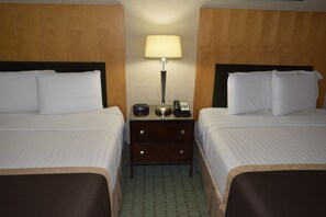 A hotel room with two beds, a nightstand with a lamp, a phone, and a small table.