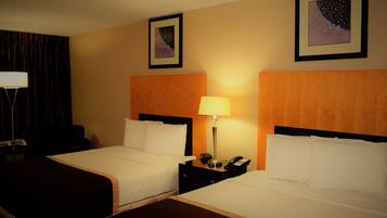 A hotel room with two beds, a nightstand with a lamp, a telephone, and two framed pictures on the wall.
