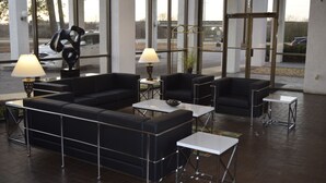 A modern lobby with black leather sofas, white tables, and lamps. Large windows offer views of parked cars and trees. - The Landmark Inn (Hartsville)