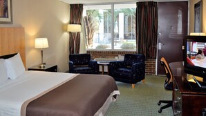 A hotel room with a bed, two armchairs, a small table, a desk with a TV, and a window with curtains. - The Landmark Inn (Hartsville)