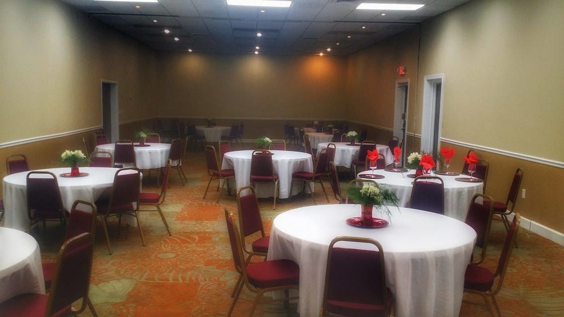 A conference room with multiple round tables, each with a white tablecloth and red chairs.
