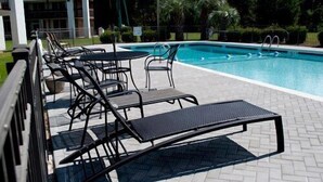 A poolside area with lounge chairs and a table, surrounded by a brick patio and greenery. - The Landmark Inn (Hartsville)