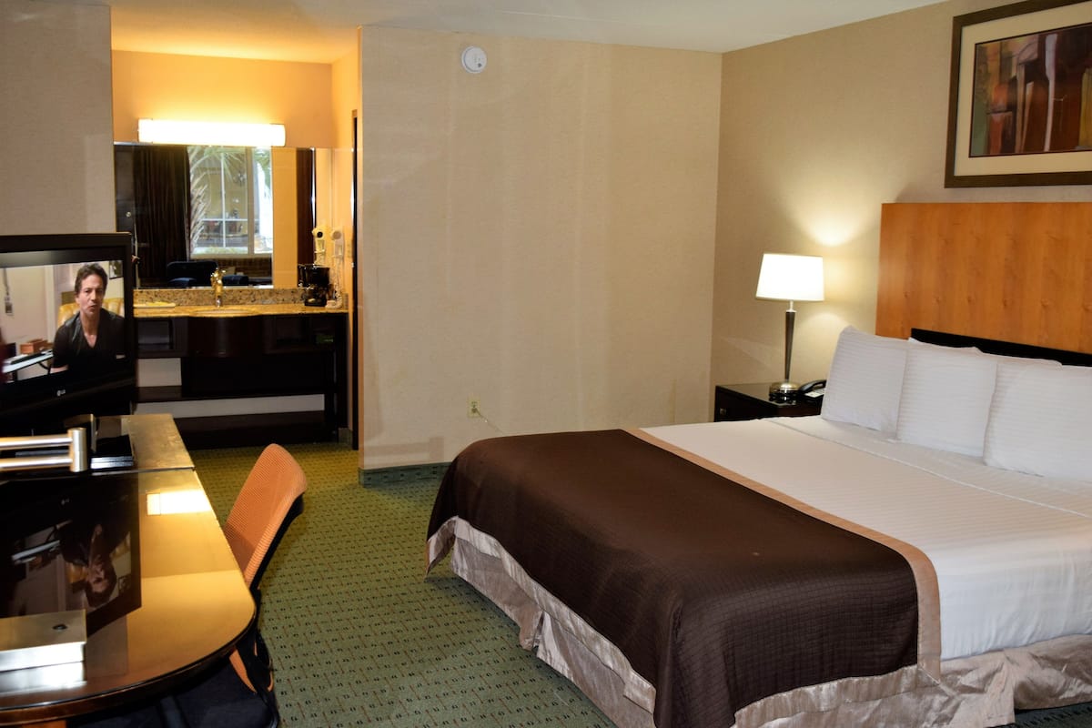 A hotel room with a bed, a desk, a chair, a TV, and a bathroom visible through an open door.