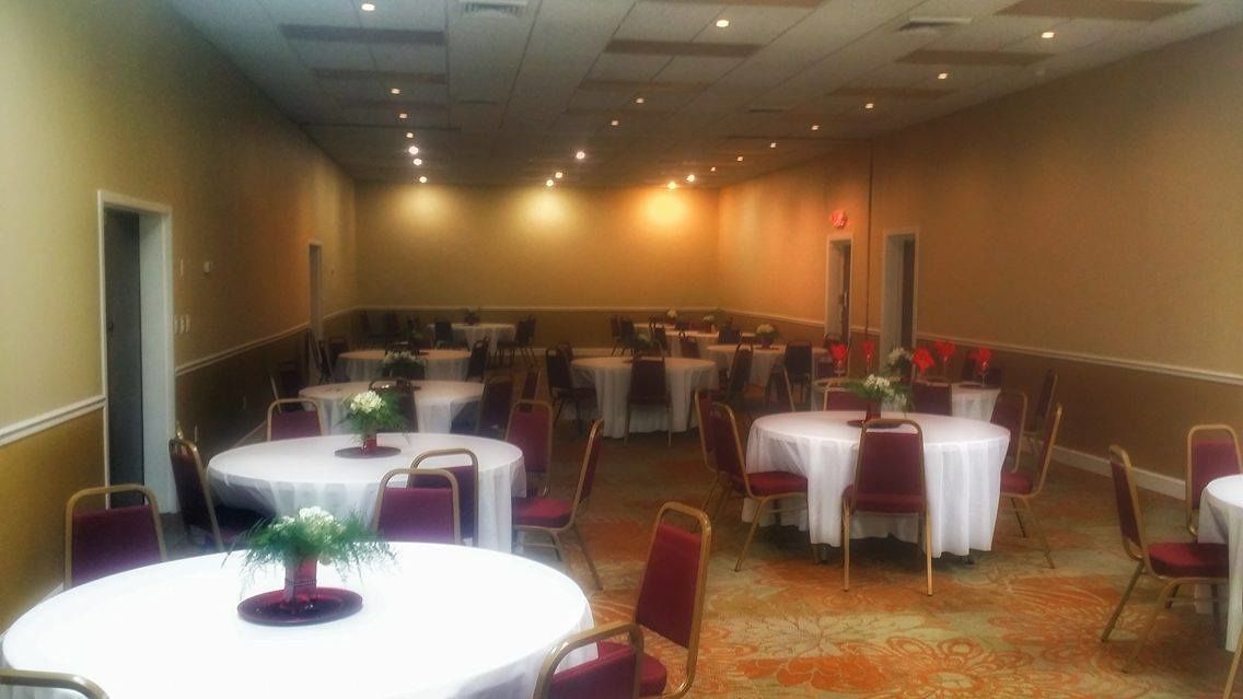 Un salón de conferencias con mesas y sillas redondas, piso alfombrado y una puerta a la izquierda.