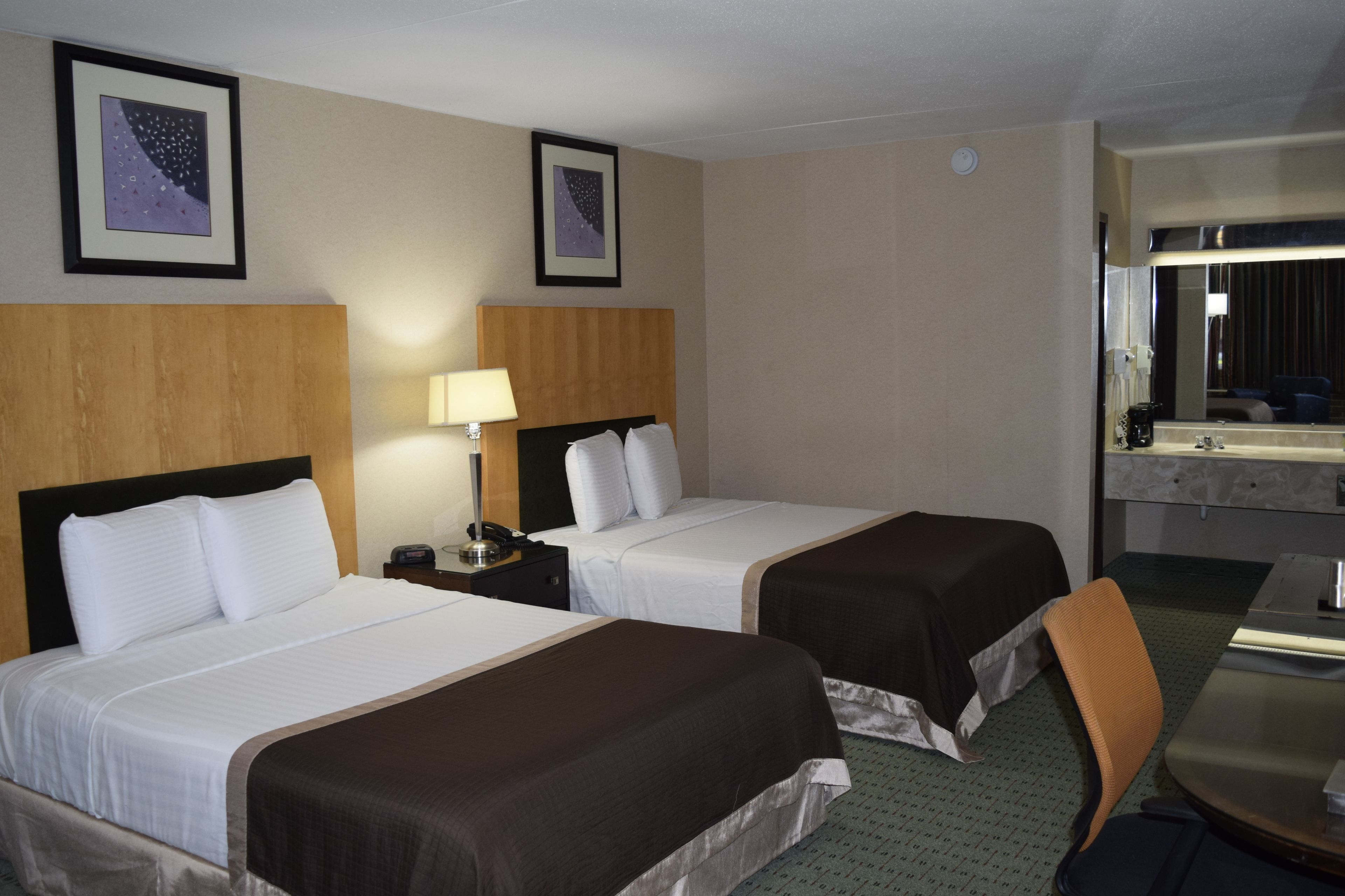 A hotel room with two beds, a desk, a chair, and a bathroom with a mirror.
