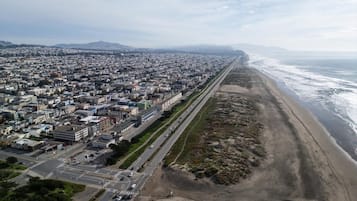 An aerial view of a coastal city with a long beachfront, a dense urban area with buildings and roads, and a clear sky.