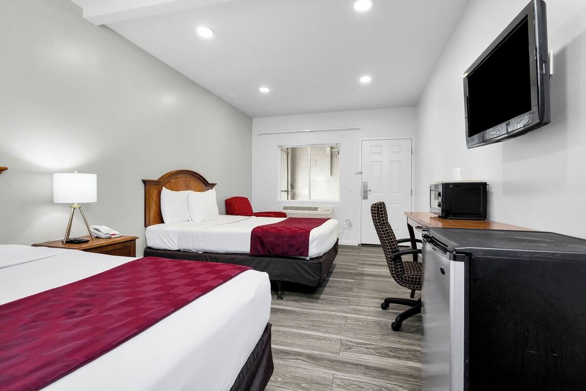 Habitación de hotel con dos camas, un escritorio con televisor, una silla y un refrigerador.