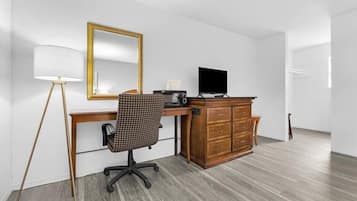 A room with a wooden desk, a chair, a television, a dresser, and a lamp.