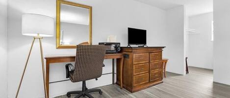 A room with a wooden desk, a chair, a television, a dresser, and a lamp.