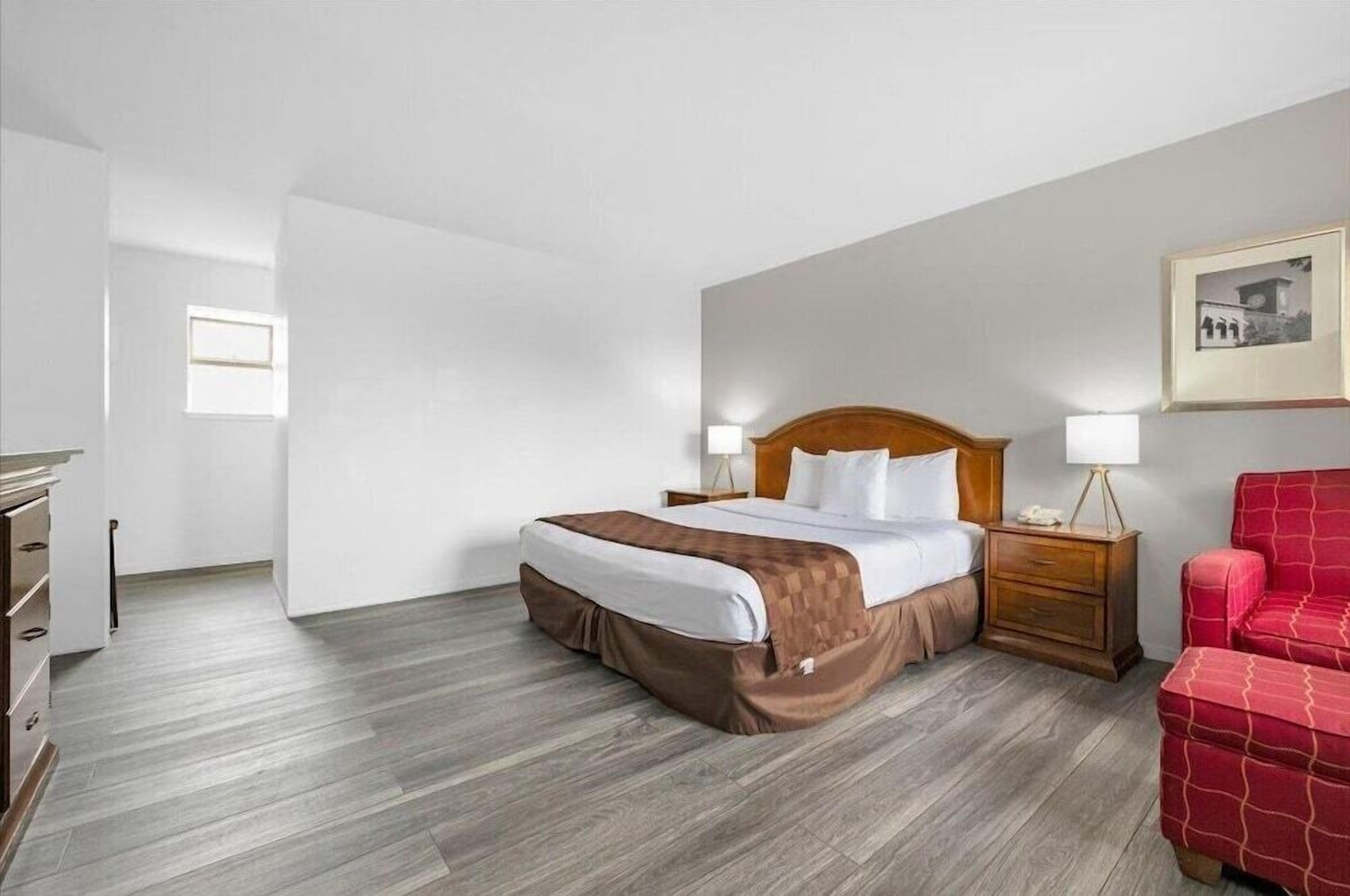 A hotel room with a bed, bedside tables, a red chair, and a framed picture on the wall.
