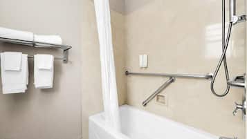 A bathroom with a bathtub, a shower, a towel rack with towels, and a handrail.