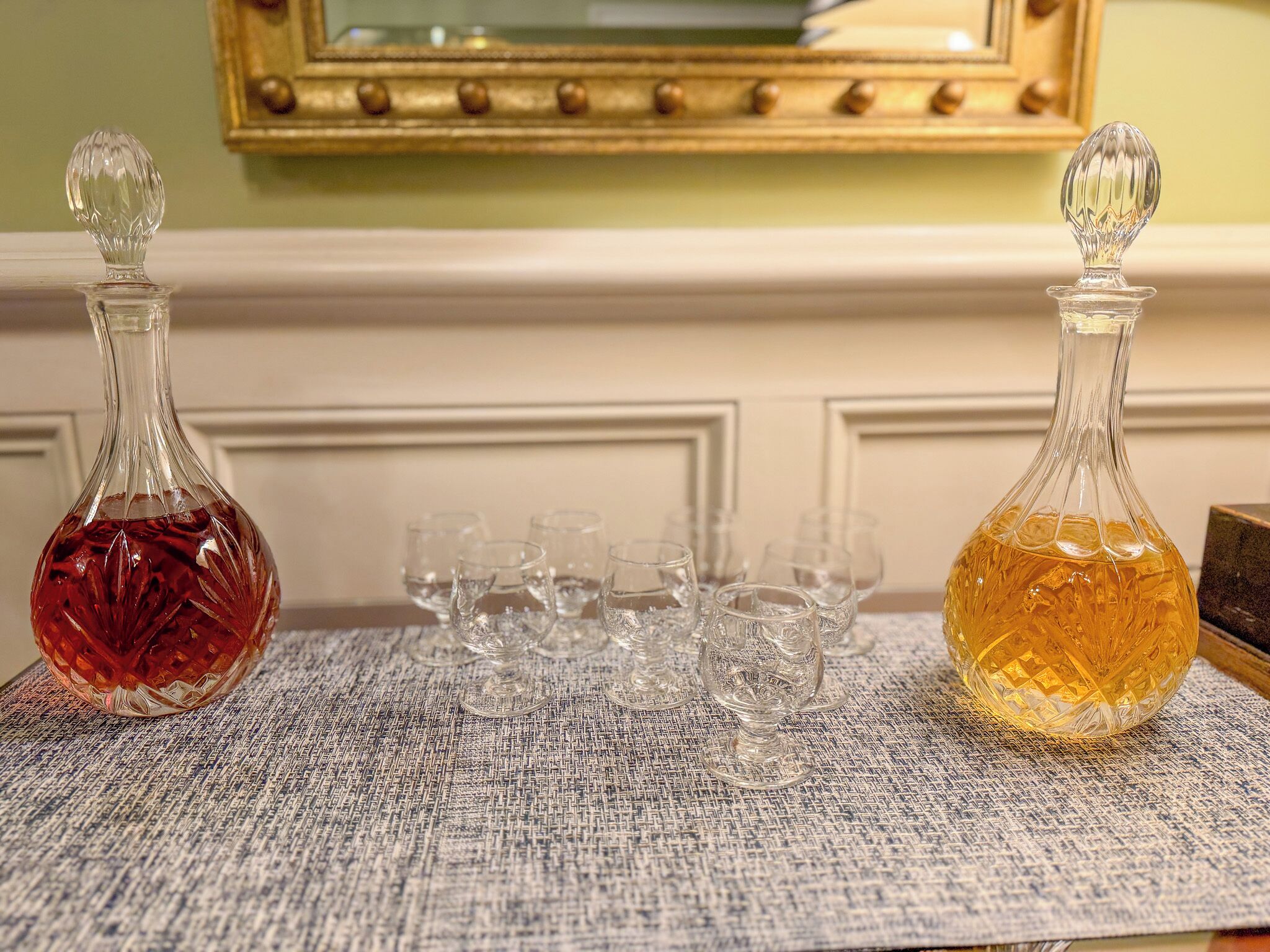 Two glass decanters on a textured tablecloth with several empty glasses.