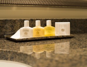 Toiletries are arranged on a countertop, featuring a body lotion, applier shampoo, and shampoo bar.