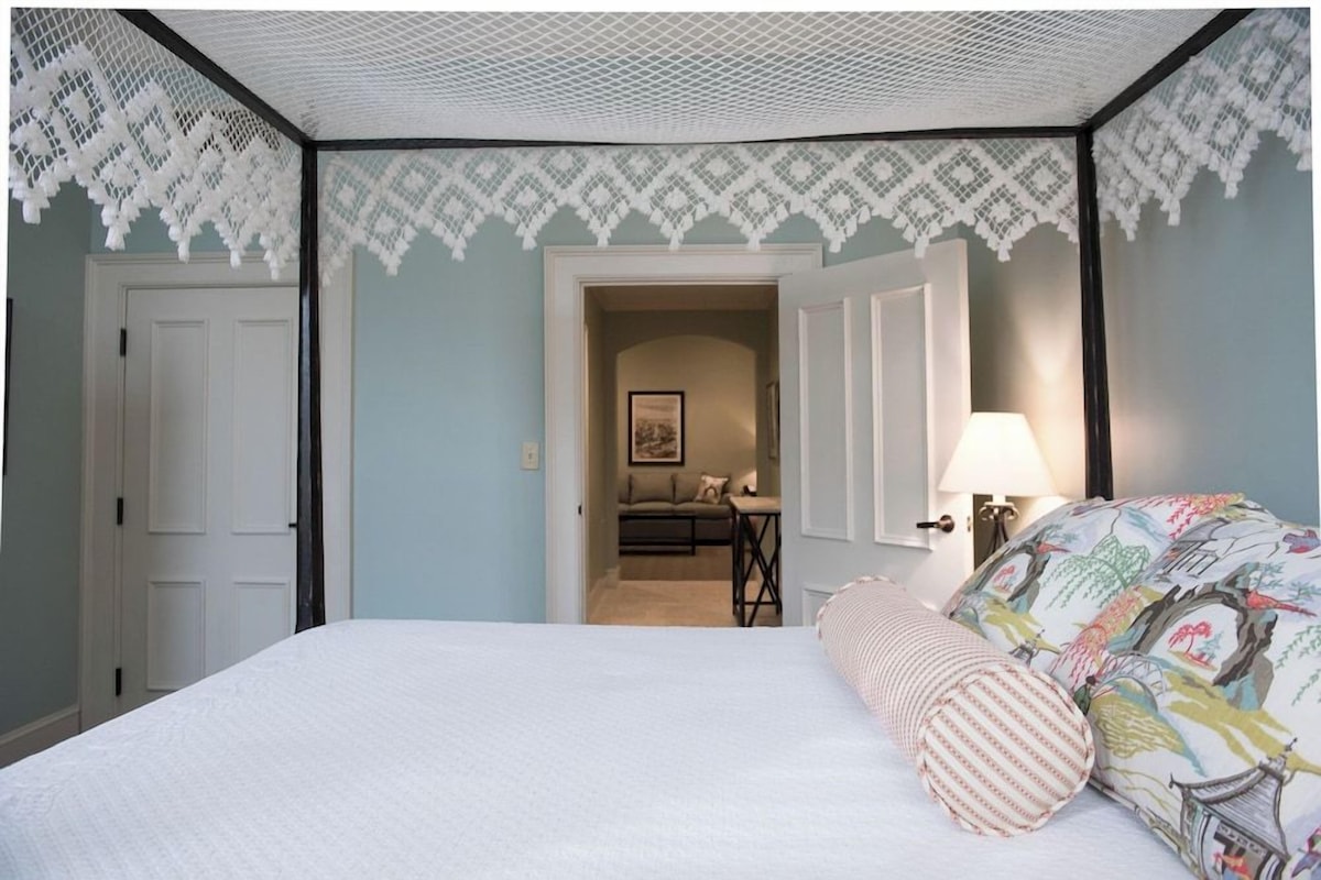 A bedroom with a bed, a nightstand, a lamp, and a door leading to another room.