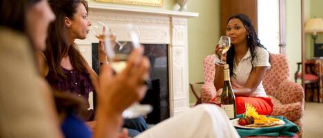 A group of people in a living room with a fireplace, a dining table with food, and a bottle of wine.