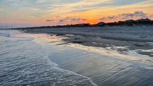 Een strand bij zonsondergang, met kalm water en gebouwen in de verte.