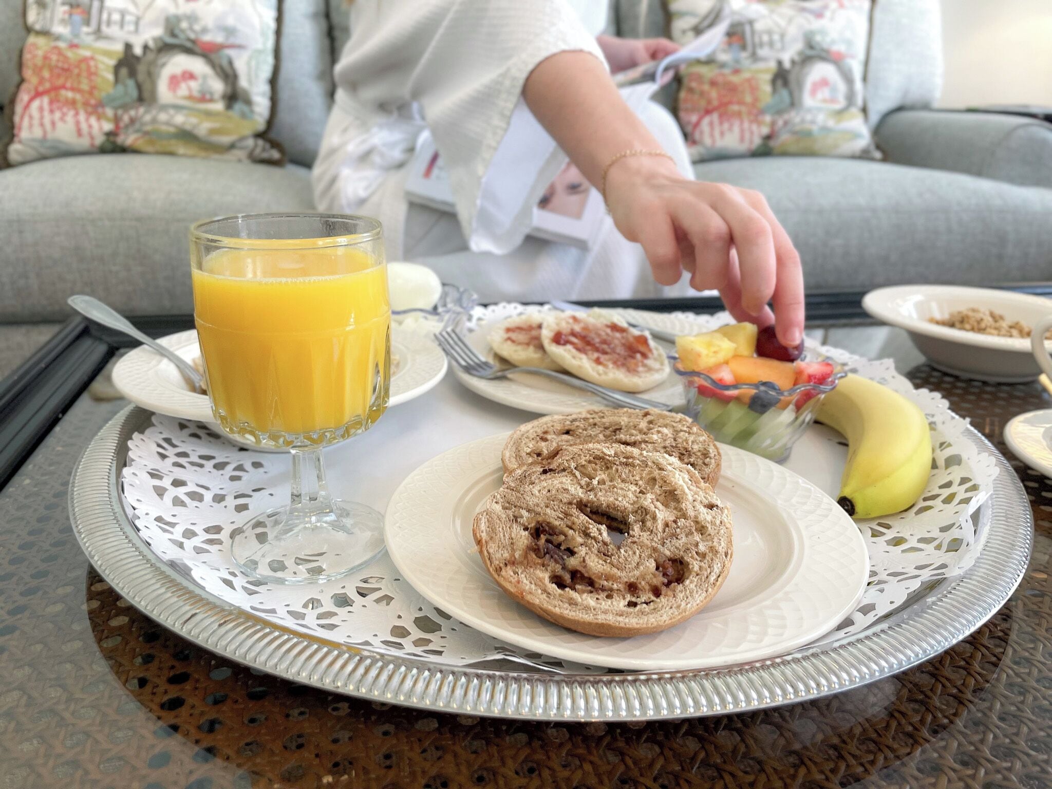 Una bandeja de desayuno con un vaso de jugo de naranja, un bagel, un plátano y un plato con ensalada de frutas sobre una mesa.