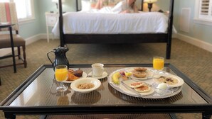 Een ontbijttafel met croissants, muffins en fruit, en een bed met een persoon op de achtergrond.