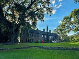 A historic brick building with large trees and a well-maintained lawn.