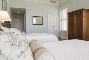 Two single beds with white bedding and decorative pillows, a wardrobe, and a framed map adorn this traditional room.