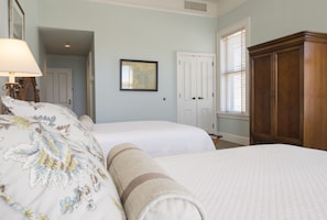 Two single beds with white bedding and decorative pillows, a wardrobe, and a framed map adorn this traditional room.