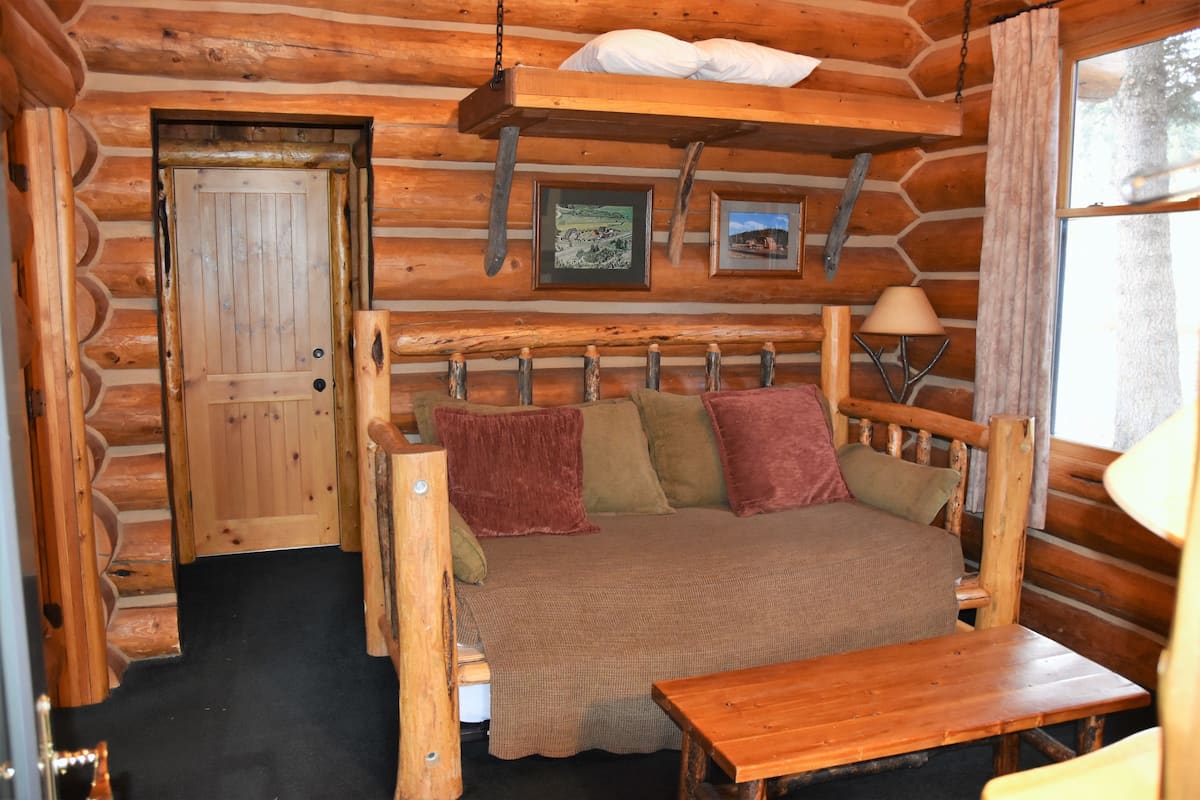 Une chambre dans une cabane en rondins, avec un lit, une table en bois et une fenêtre.